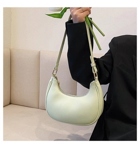 Detail of mint green crescent bag with gold hardware and adjustable strap held by model