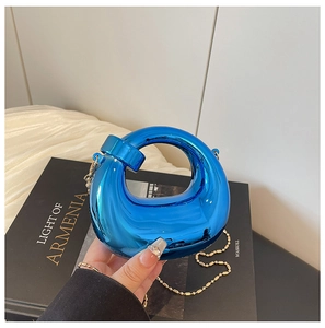 Dettaglio della borsa clutch in acrilico blu specchiato con catena dorata su libro