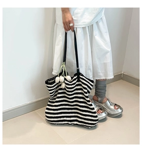 Detail of hand-woven striped tote bag with black leather straps in a minimalist setting