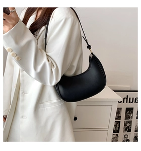 Detail of a black leather half-moon hobo bag with adjustable strap on a white blazer