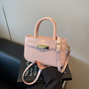 Pink faux crocodile leather handbag with gold clasp on black art books background