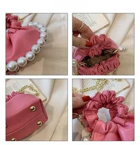Detail of pink pleated cloud bag featuring large pearl handle and gold chain strap