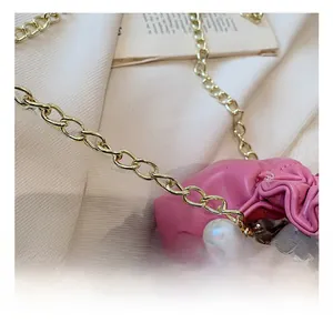 Detail of pink dumpling bag featuring large pearls and gold chain strap on soft texture