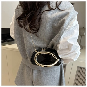 Detail of black patent leather evening bag with large gold circular metal handle and chain