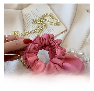 Detail of pink ruched cloud bag featuring decorative pearls and gold chain strap