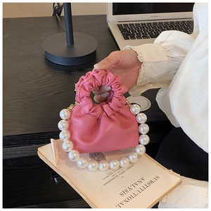 Detail of pink pleated mini bag featuring elegant oversized pearl handle on dark desk