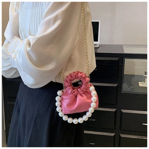 Detail of pink pleated cloud bag featuring large pearl handle and gold chain strap