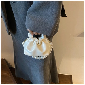 Close-up of white ruched cloud handbag with decorative oversized pearl chain strap