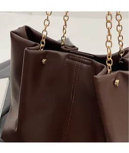 Detailansicht der braunen Ledertasche mit goldener Kette und feiner vertikaler Steppnaht