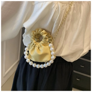 Detail of a mini yellow cloud bag showing soft pleated texture and large pearl handle