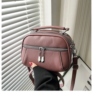 Detail of pink faux leather crossbody bag showing three layered zipper compartments
