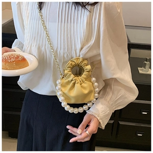 Detail of yellow mini pleated cloud bag featuring a large pearl handle and gold chain strap