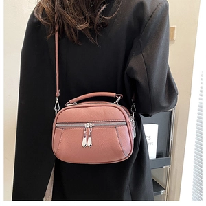 Dusty pink soft leather shoulder bag with double zippers worn over a black blazer