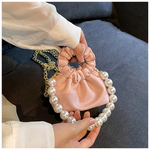 Detail of pink ruched cloud bag featuring large pearl handle and gold chain strap