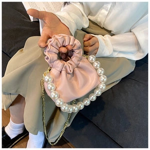 Detail of pink pleated cloud bag with oversized pearl handle and gold chain strap