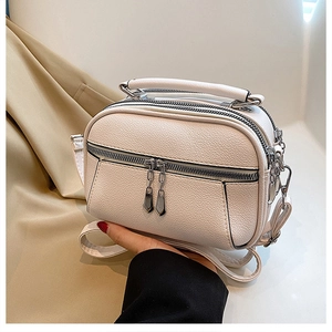Detail of white textured PU leather crossbody bag with multiple silver zippers and handle