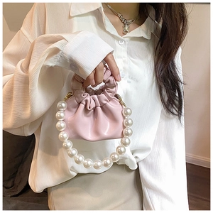 Pink pleated cloud bag with large pearl handle carried by model in white shirt