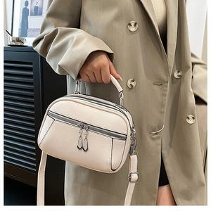Detail of cream soft leather crossbody bag showing litchi texture and multi-zipper layers