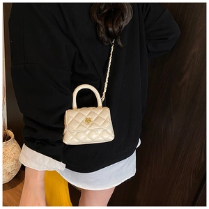 Detail of cream mini quilted handbag with gold flower clasp and chain strap on model