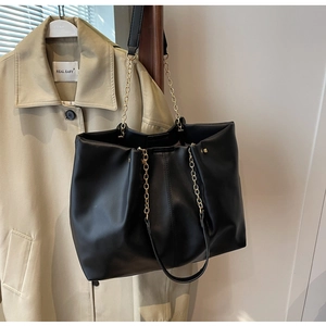 Detail einer weichen schwarzen Leder-Tote mit goldener Kette auf einem beigen Trenchcoat
