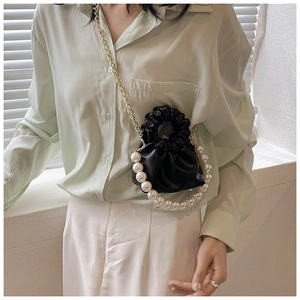 Close-up of black pleated cloud bag featuring a large pearl handle and gold chain strap