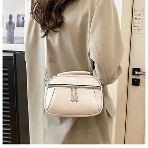 Detailed view of cream leather crossbody bag with lychee texture and dual silver zippers