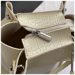Detail of crocodile pattern texture on cream handbag with silver metal zipper closure