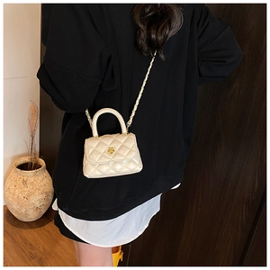 Detail of a mini quilted crossbody bag with a gold flower clasp on a beige leather texture