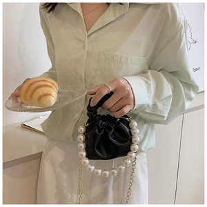 Detail of mini black pleated bag featuring large pearl handle and gold chain strap