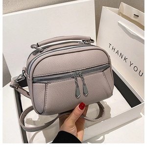 Detail view of light purple textured leather crossbody bag with three zipper compartments
