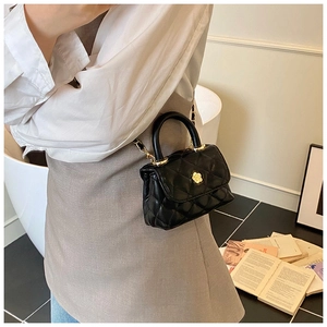 Detailed view of black quilted mini bag with gold flower clasp and chain strap on a model