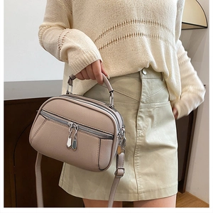 Detail view of beige soft leather crossbody bag with dual zippers and silver hardware