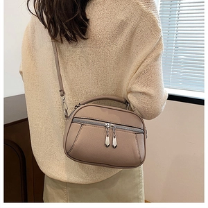 Macro view of beige lychee textured leather crossbody bag with dual metal zipper details