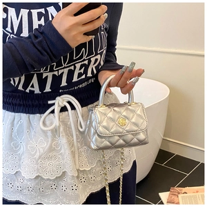 Detail of silver quilted mini bag with floral clasp and metal chain strap held by model