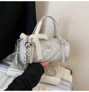 Detail of grey quilted cylinder bag with chain strap and lace bow decoration