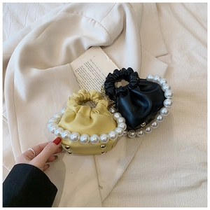 Detail of mini pleated cloud bags with large pearl handles in yellow and black leather