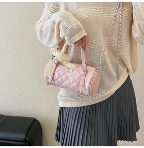 Detail of pink quilted cylinder bag featuring a white lace bow and silver chain strap