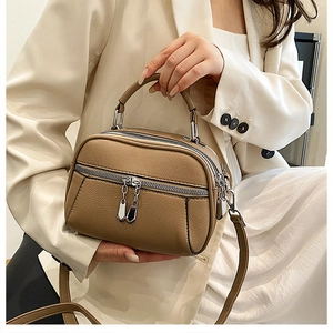Detail view of brown lychee grain leather crossbody bag with dual silver zippers