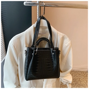 Detail of black crocodile texture bag with silver circular metal handle on white suit background