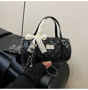 Detail of black quilted cylindrical bag with silver lock and cream lace bow accessory