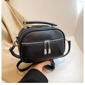 Close-up of black pebble leather crossbody bag with triple zipper layers and silver hardware