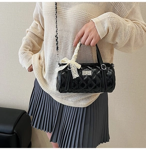 Detail of black quilted cylindrical bag with silver twist lock and lace bow handle