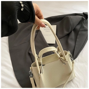 Detailed close-up of cream crocodile pattern handbag with metal hardware and top handle