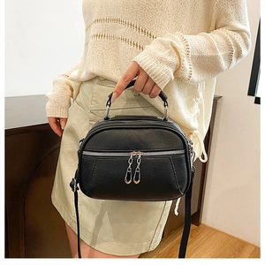 Detail view of black lychee grain leather crossbody bag with triple silver zipper design
