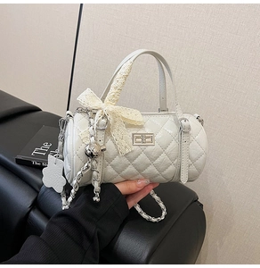Close-up of quilted white cylinder bag with lace bow and silver twist lock detail