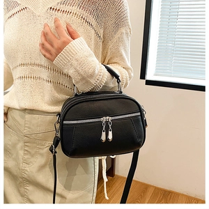 Detail of black pebbled leather crossbody bag with silver zippers on white knit outfit