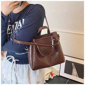 Detail of dark brown crocodile embossed leather handbag with metal ring handles