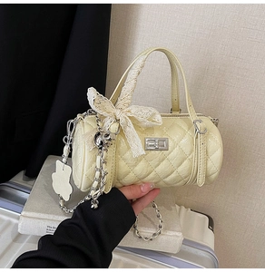 Detail of quilted cream cylinder bag with silver turn-lock, lace bow and bear charm