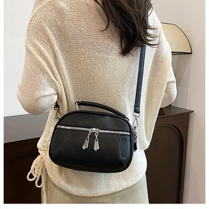 Rear view of model wearing a black pebbled leather crossbody bag with dual silver zippers
