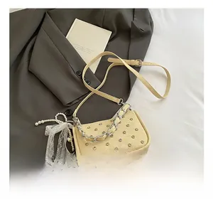 Detail of beige rivet handbag with chunky silver chain and pearl bow charm accessory